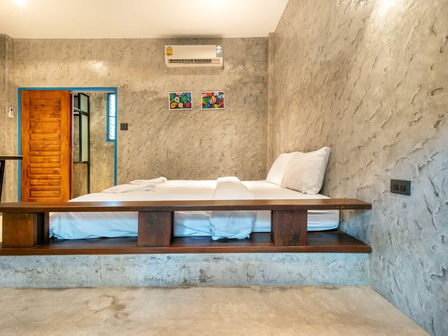 Un dormitorio con una cama, un banco de madera, una puerta y un aire acondicionado instalado en la pared.