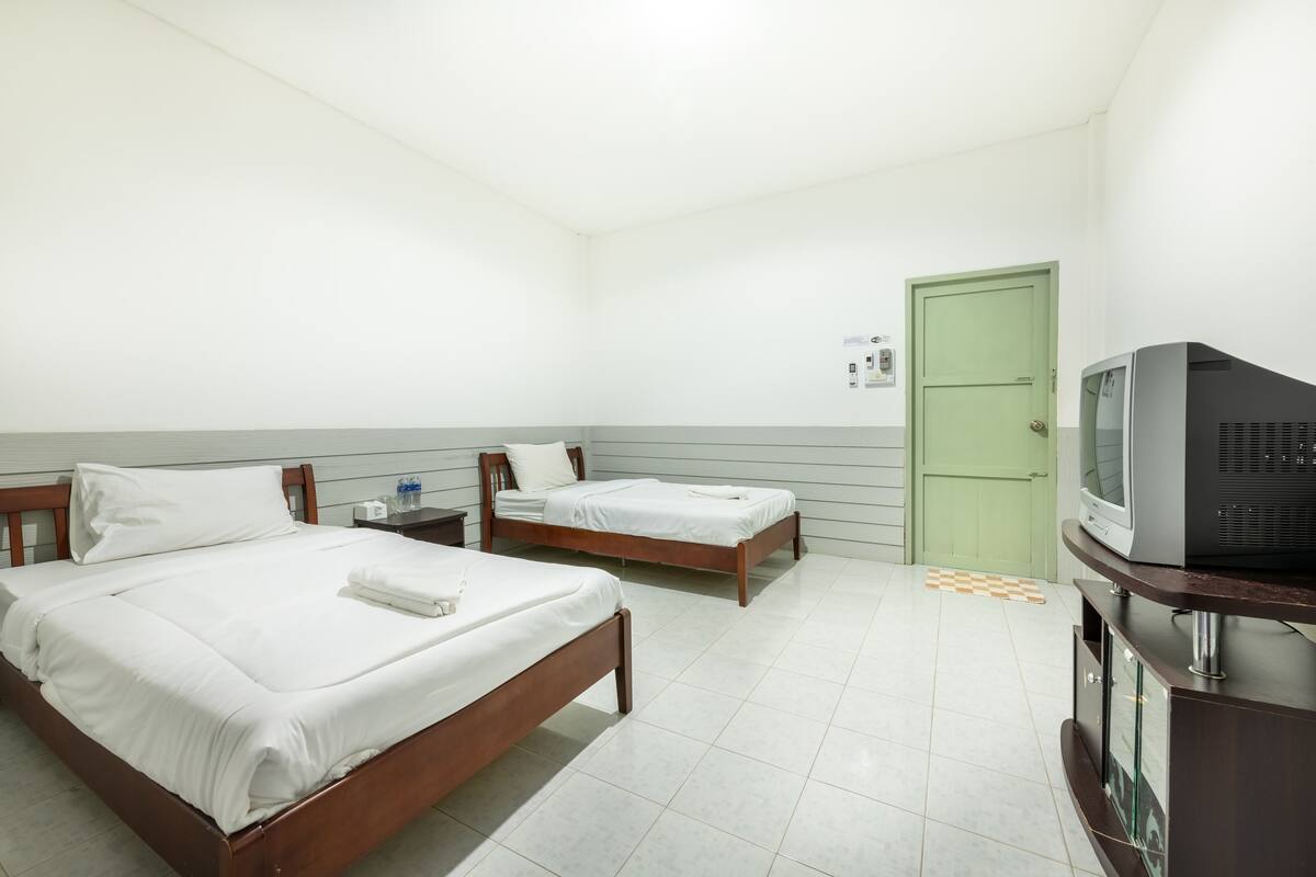 A hotel room with two single beds, a television, and a green door.