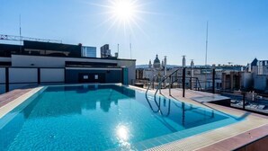A rooftop swimming pool with clear blue water, a sun shining in the background, and a cityscape view. - SWU Magazine Rooms (Budapest)
