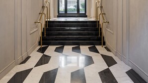 A grand hallway with a black and white checkered floor, a central staircase with gold railings, and a circular light fixture on the ceiling. - SWU Magazine Rooms (Budapest)