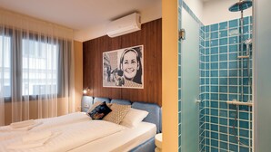 A hotel room with a bed, a shower with blue tiles, and a picture on the wall. - SWU Magazine Rooms (Budapest)