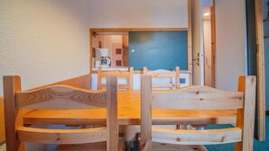 Una mesa de madera con sillas en una habitación con pared blanca y puerta azul.