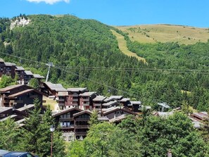 Una località montana con edifici in stile chalet, una seggiovia e uno sfondo boscoso.