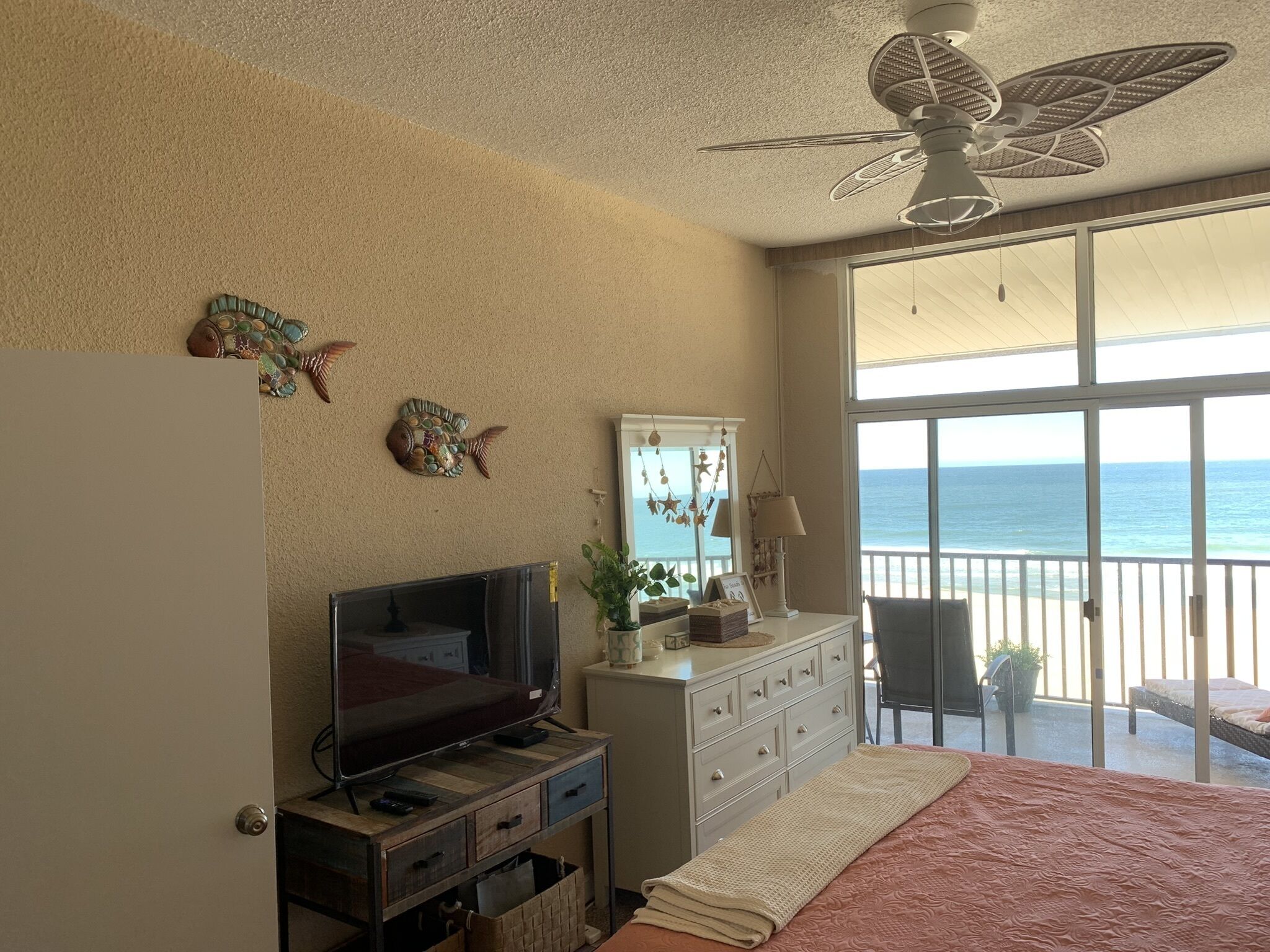 A bedroom with a TV, dresser, and a balcony with a view of the ocean.