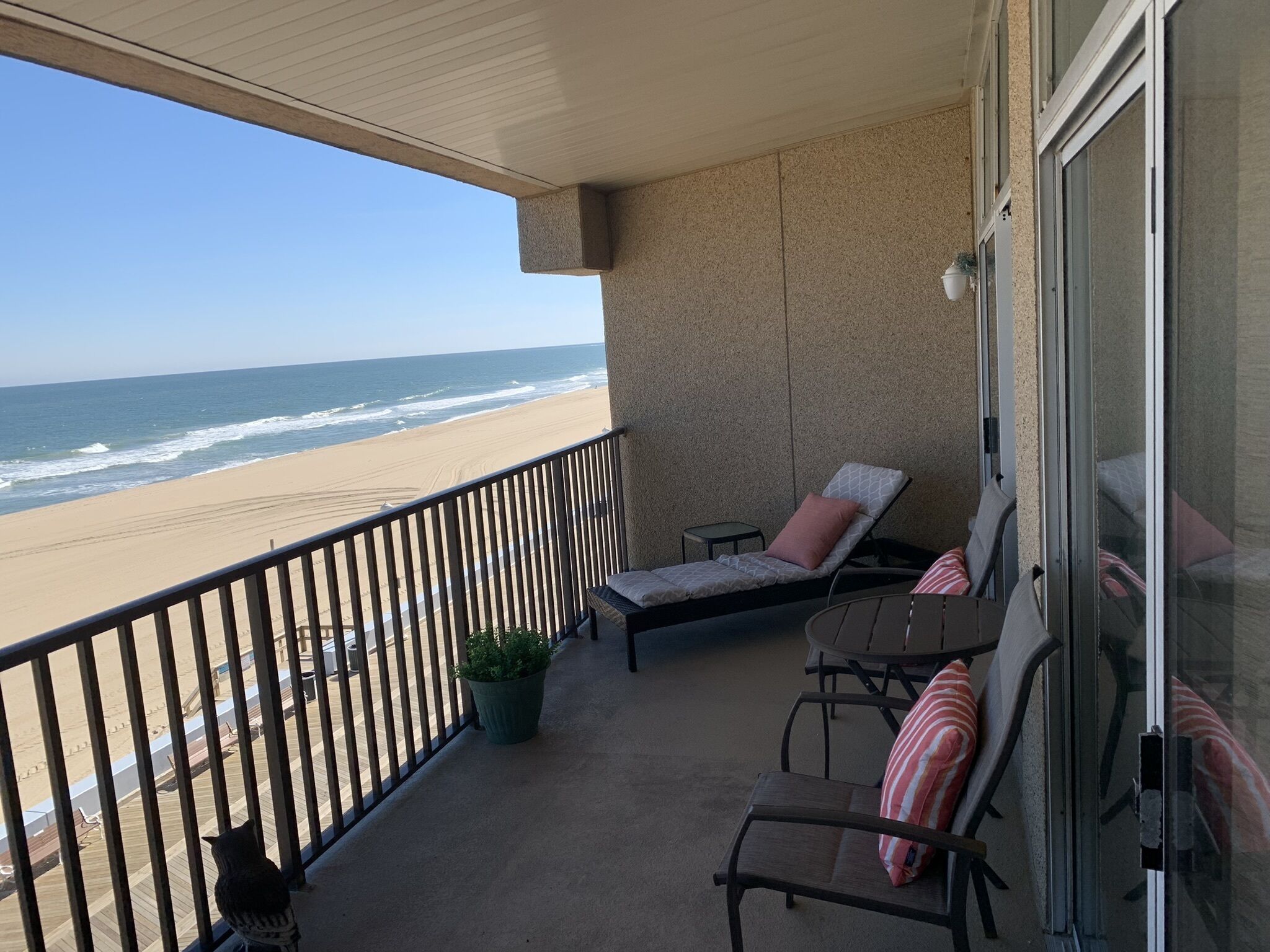 A balcony with a view of the beach, two lounge chairs, a small table, and a potted plant.