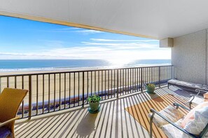 Un balcon donnant sur la plage, agrémenté de deux plantes en pot et d’un espace détente avec une table et des chaises.