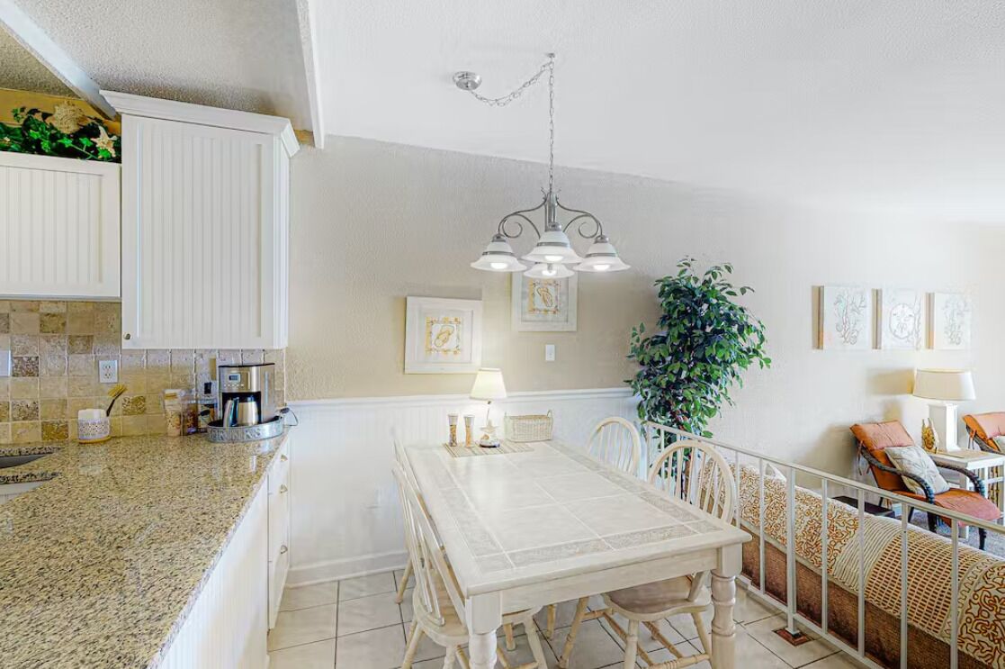 Un coin repas avec une table et des chaises blanches, un luminaire suspendu et une plante en pot.