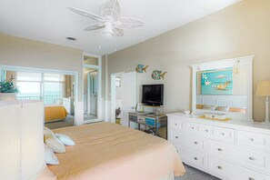A hotel room with a bed, a TV, a dresser, and a view of the ocean.