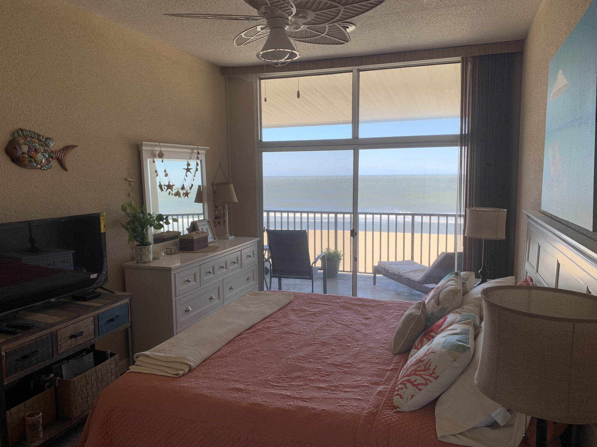 Une chambre d’hôtel avec un grand lit, une télévision, une commode et un balcon donnant sur la plage.