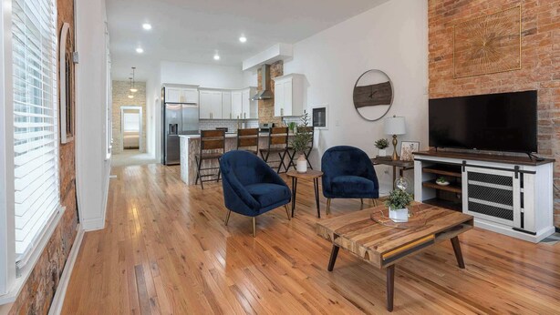 A modern living room with a wooden floor, a TV, and blue chairs.