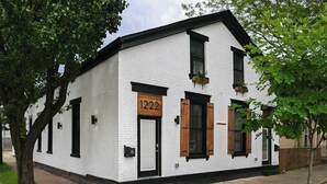 A white building with black trim, a wooden door, and a number sign "1222".