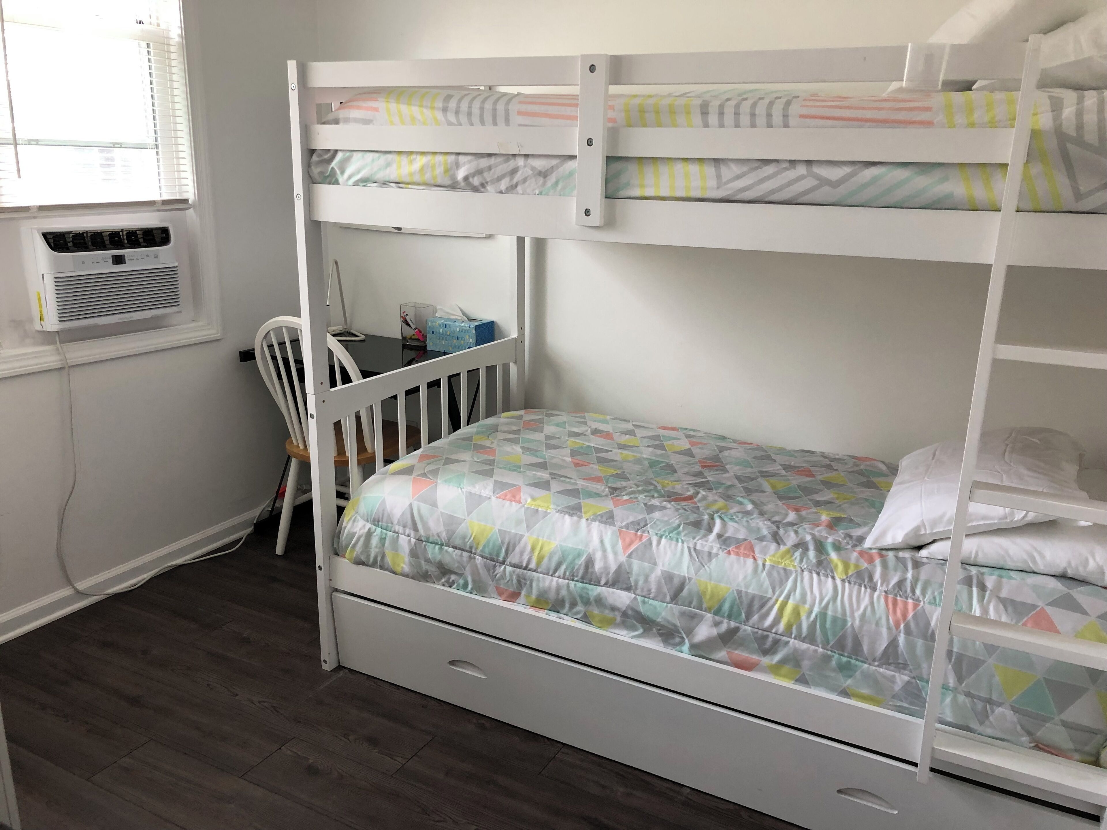 Una cama litera con una cama inferior, un escritorio con una silla y un equipo de aire acondicionado.