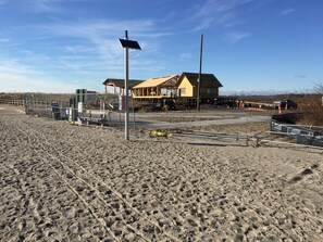 Ein sandiger Strand mit einer Holzkonstruktion und einem Haus im Hintergrund.