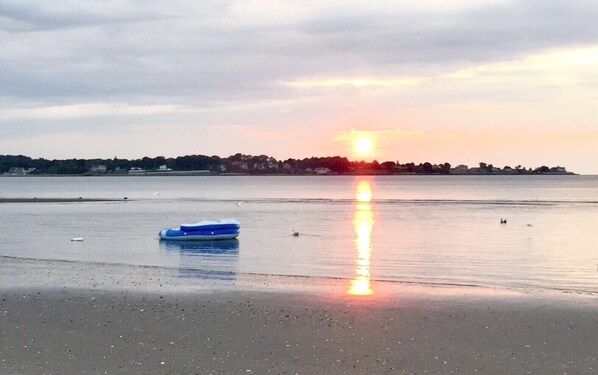 Ein Strand mit einem Boot und ruhigem Wasser, das den Sonnenuntergang widerspiegelt.