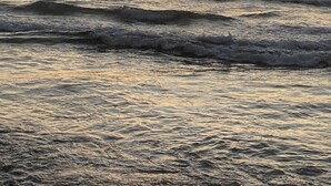A beach with waves and a sunset in the background. - House 30 meters from Pernambuco Beach (Guarujá)