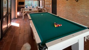 A pool table in a room with brick walls, mounted animal skulls, and hanging pendant lights. - House 30 meters from Pernambuco Beach (Guarujá)