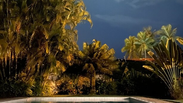 A swimming pool surrounded by palm trees at dusk. - House 30 meters from Pernambuco Beach (Guarujá)