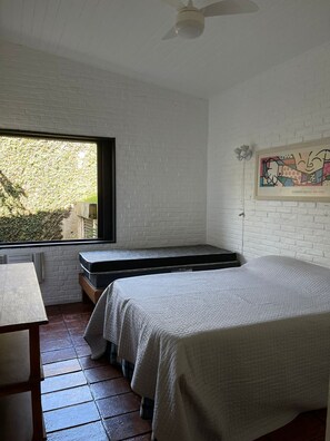 A bedroom with two beds, a window, a ceiling fan, and a painting on the wall.