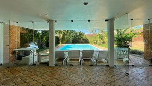 An outdoor pool area with a barbecue setup and lounge chairs. - House 30 meters from Pernambuco Beach (Guarujá)