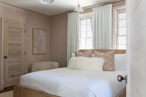 A bedroom with a bed, a door, a window with curtains, and a wall-mounted picture.