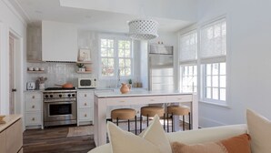 Una cocina moderna con armarios blancos, una isla central con taburetes, un refrigerador de acero inoxidable y un colgante de luz.