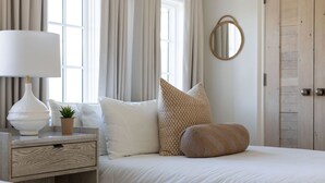 Un dormitorio ordenado con cama, mesita de noche con lámpara, una planta pequeña y un espejo en la pared.