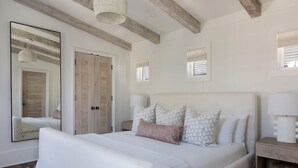 A bedroom with a large bed, a wooden wardrobe, a bedside table, and a mirror.