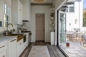 Una cocina moderna con armarios blancos, una puerta de madera y vistas a un patio exterior con mobiliario de mimbre.