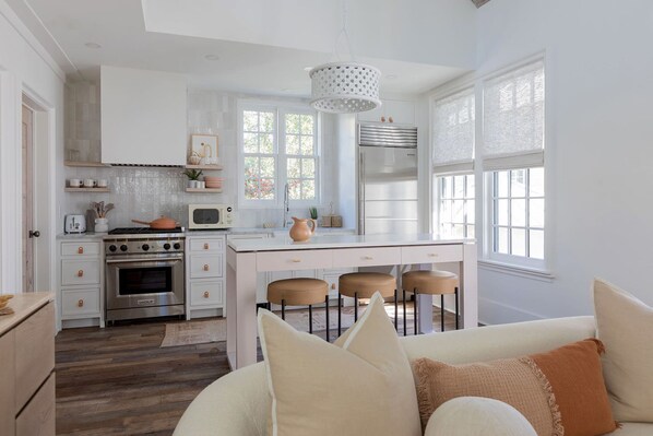 Una cocina moderna con armarios blancos, una isla central con taburetes, un refrigerador de acero inoxidable y un colgante de luz.