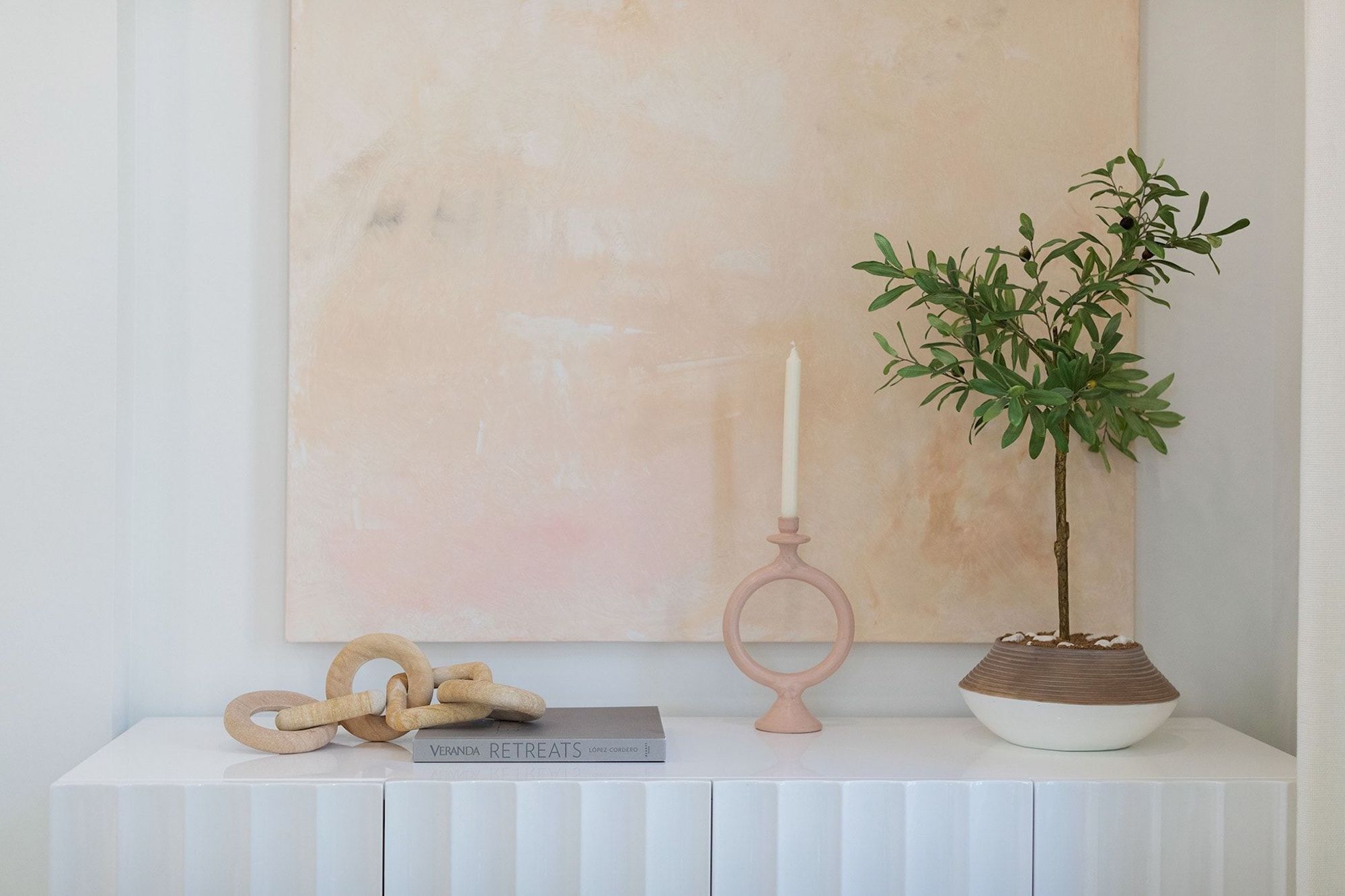 Una consola blanca con una planta en maceta, una vela y un libro titulado 'VERANDA RETREATS'.