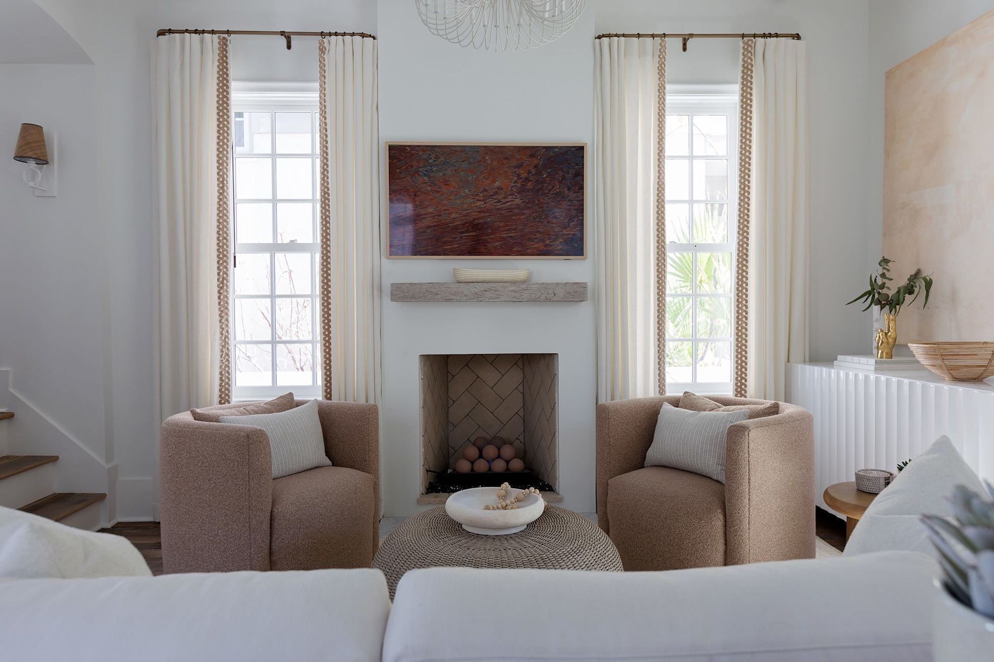 Un salón con dos sillones beiges, un sofá blanco, una chimenea y un cuadro abstracto grande sobre ella.