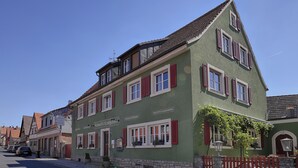 Ein traditionelles europäisches Gebäude mit grüner Fassade, roten Fensterläden und einem Steinsockel.