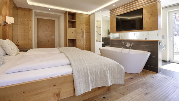Ein modernes Schlafzimmer mit einem großen Bett, einer freistehenden Badewanne, Holzverkleidung und einem Flachbildfernseher über dem Waschbecken.