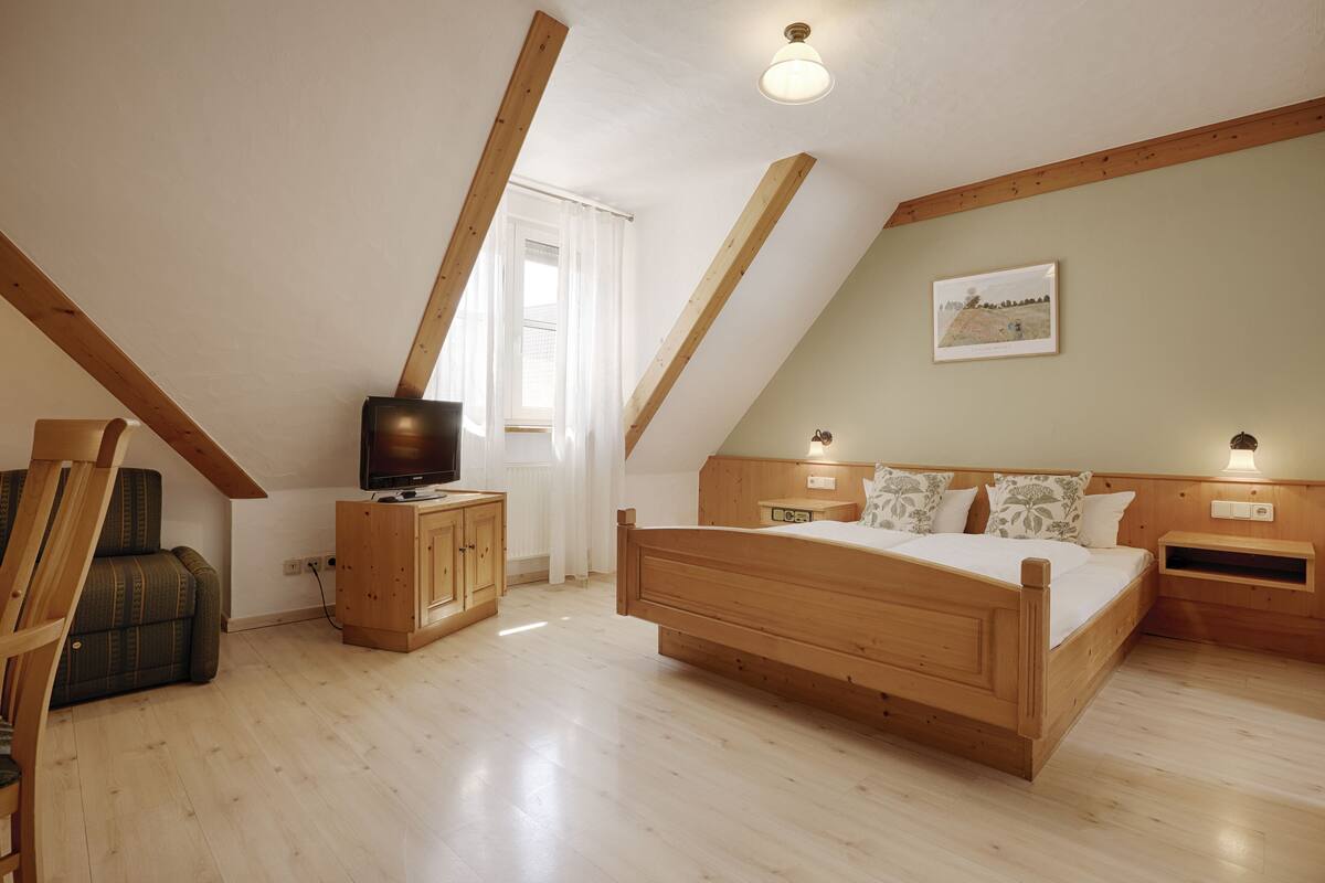 Quarto com cama de madeira, televisão sobre um armário de madeira e janela com cortinas.