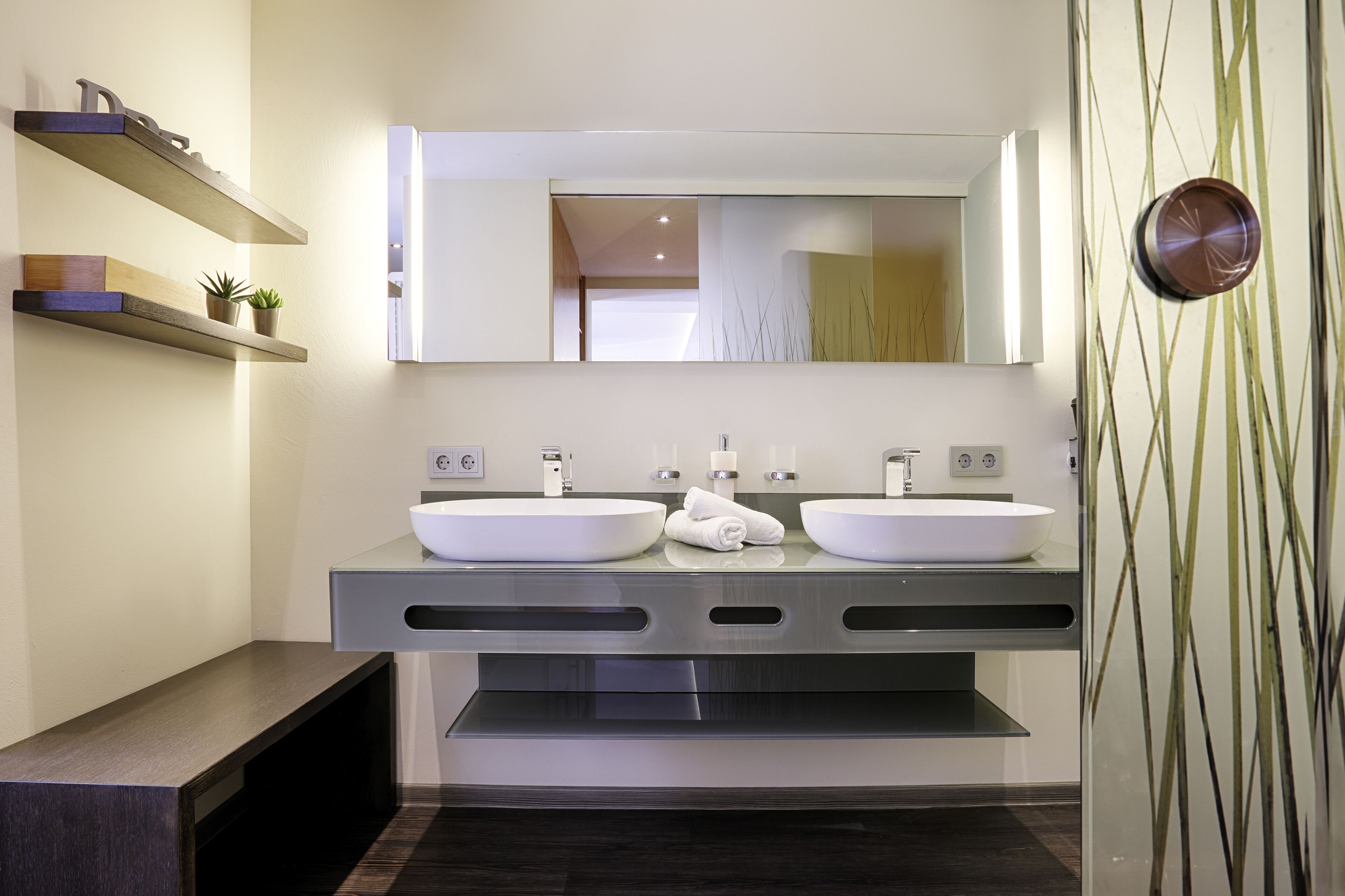 A modern bathroom with two sinks, a large mirror, and built-in shelves with plants.