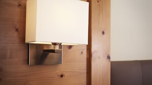 Eine Wandleuchte mit rechteckigem Lampenschirm, vor einer Holzwand mit sichtbarer Maserung und Ästen.