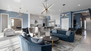 A spacious living area with a blue sofa set, a coffee table, and modern lighting fixtures. - Premium Home Near Disney w/ Speakeasy Lounge, Theater, Builder Theme BR & Gym (Davenport)