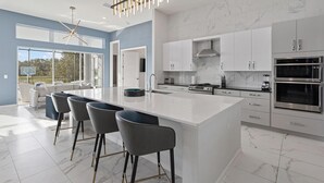 A modern kitchen with a large island, bar stools, and stainless steel appliances. - Premium Home Near Disney w/ Speakeasy Lounge, Theater, Builder Theme BR & Gym (Davenport)