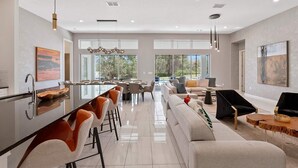 A spacious living area with a large sofa, a dining table with chairs, and a kitchen area with a bar. - Grand Home w Karaoke RM, Piggy Playhouse BR, Theater, Arcade & Gym, Near Disney (Davenport)