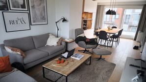 A modern living room with a grey sofa, a wooden coffee table, and a dining area with a table and chairs. - Penthouse 2 Terrassen -oostduinkerke bad (Oostduinkerke)