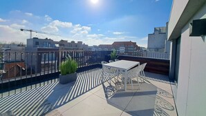 A rooftop terrace with a table and chairs, a potted plant, and a view of the cityscape. - Penthouse 2 Terrassen -oostduinkerke bad (Oostduinkerke)