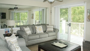 A living room with a gray sofa, a coffee table, and a ceiling fan. There is a sliding glass door leading to a balcony.
