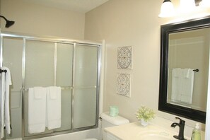 A bathroom with a glass-enclosed shower, a white sink with a black faucet, a mirror, and two decorative wall pieces. - 1409m 1 Bedroom Condo by Redawning (Calabash)