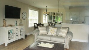 A living room with a sofa, coffee table, and a dining area with chairs and a chandelier.