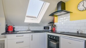 A modern kitchen with a skylight, white cabinets, a red kettle, a microwave, and a clock on the wall. - Ayla (Lyme Regis)