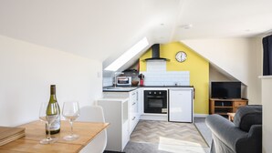 A compact kitchen with a microwave, oven, and a clock on the wall. - Ayla (Lyme Regis)