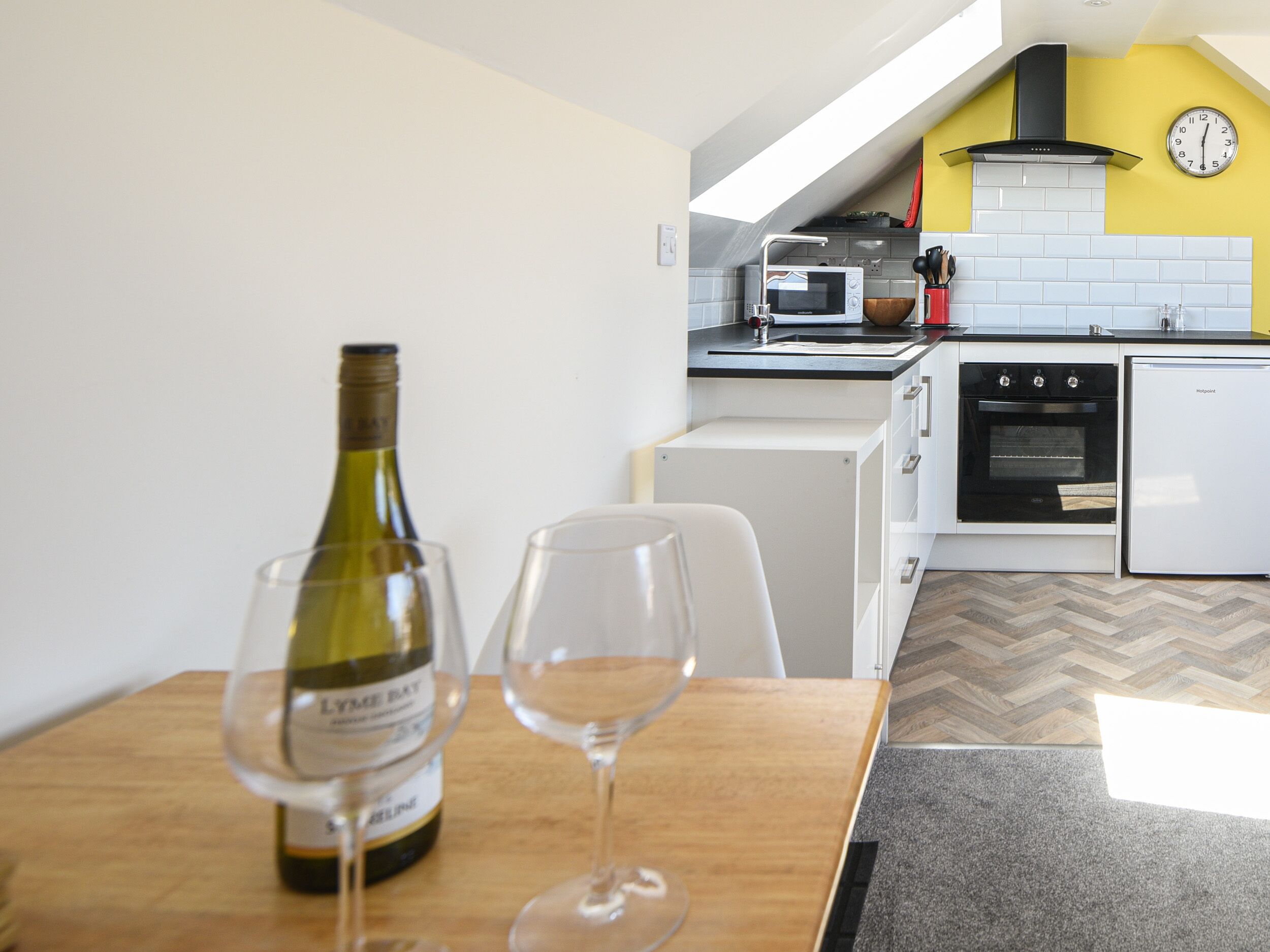 A modern kitchen with white cabinets, a microwave, a stove, and a clock on the wall.
