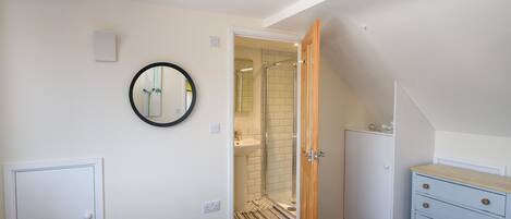 A bedroom with a bed, a dresser, a mirror, and a bathroom visible through an open door.