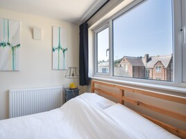 Un dormitorio con un ventanal grande, una cama, un radiador, una lámpara y dos obras de arte colgadas en la pared.