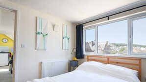 A hotel room with a bed, a radiator, a window with a view of houses, and a clock on the wall. - Ayla (Lyme Regis)